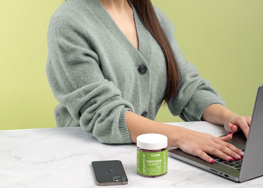 Lady working on a laptop with her container of Novomins Lions Mane gummies next to her on the table.